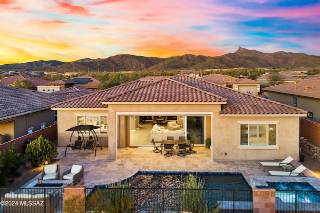 back house at dusk featuring a mountain view, a fenced in pool, and a patio