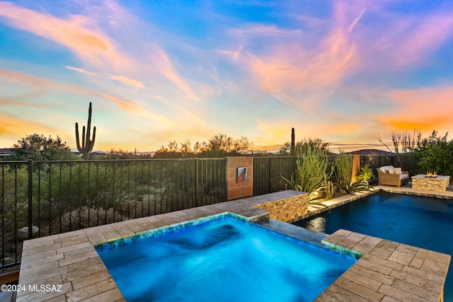 pool at dusk featuring pool water feature, a patio, and a hot tub