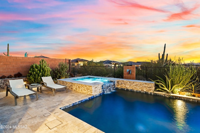 pool at dusk featuring an in ground hot tub and a patio area