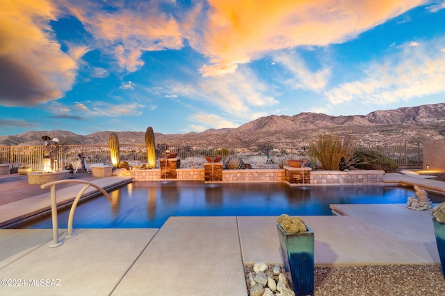 pool at dusk with a mountain view, a patio, and a fire pit