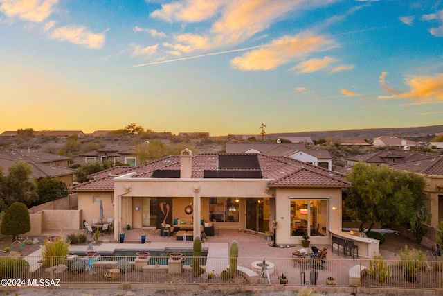 back house at dusk featuring an outdoor living space, solar panels, exterior bar, and a patio