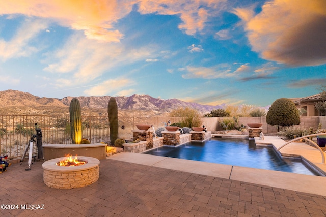 pool at dusk featuring a mountain view, pool water feature, a patio, and an outdoor fire pit