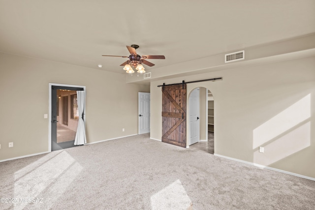 carpeted empty room featuring ceiling fan and a barn door