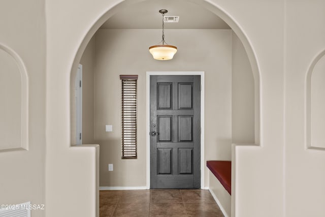 foyer entrance with baseboards, arched walkways, dark tile patterned floors, and visible vents