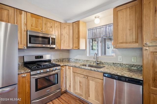 kitchen featuring stainless steel appliances, light stone counters, light hardwood / wood-style floors, and sink