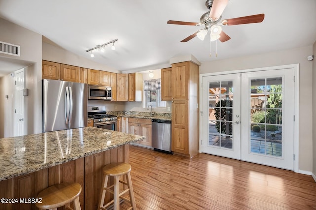 kitchen featuring light stone countertops, light wood-type flooring, stainless steel appliances, and french doors