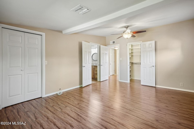 unfurnished bedroom featuring ceiling fan, beam ceiling, wood-type flooring, and connected bathroom