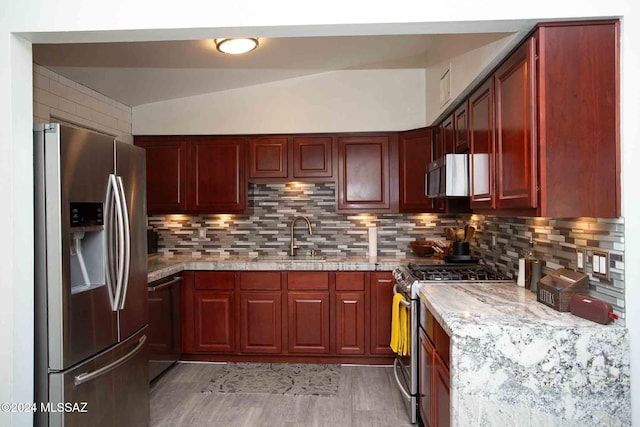 kitchen featuring tasteful backsplash, light stone countertops, stainless steel appliances, and vaulted ceiling