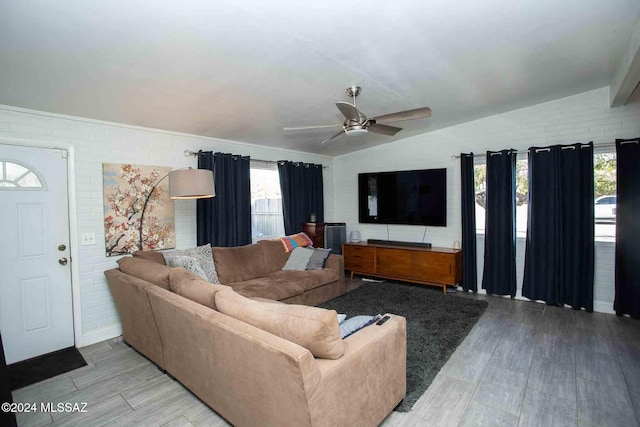 living room with plenty of natural light, brick wall, vaulted ceiling, and light wood-type flooring