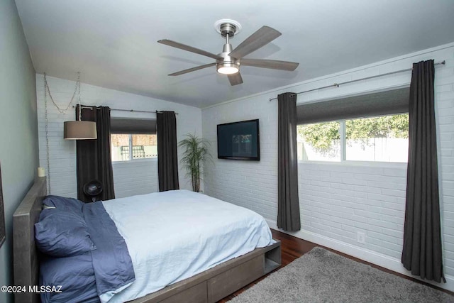 bedroom featuring ceiling fan, brick wall, dark hardwood / wood-style floors, and lofted ceiling