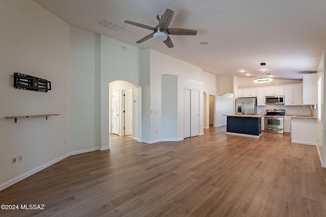 unfurnished living room with ceiling fan, high vaulted ceiling, sink, and light wood-type flooring