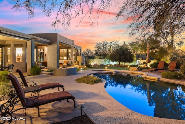 pool at dusk featuring a patio area and a hot tub