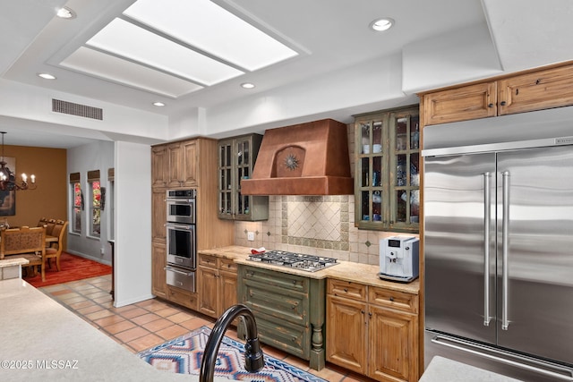 kitchen with tasteful backsplash, light tile patterned floors, custom exhaust hood, a chandelier, and appliances with stainless steel finishes