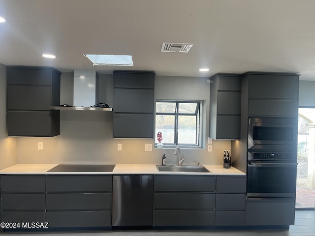 kitchen featuring black appliances, sink, a skylight, wall chimney exhaust hood, and gray cabinets