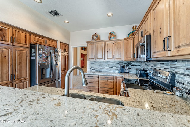 kitchen featuring sink, light stone countertops, a textured ceiling, appliances with stainless steel finishes, and tasteful backsplash