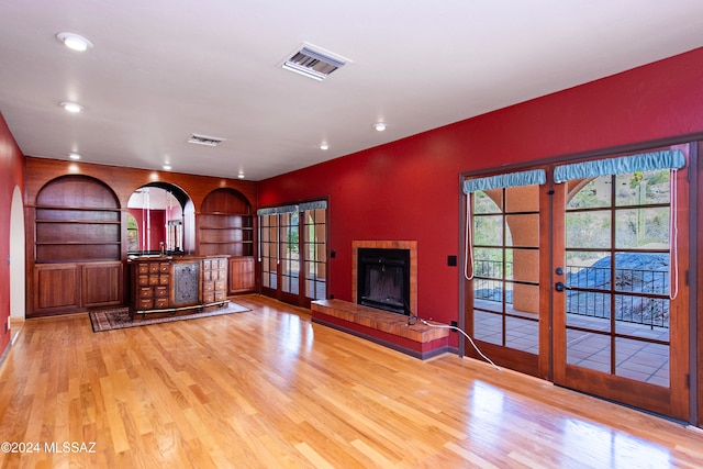 unfurnished living room with built in shelves, french doors, light hardwood / wood-style floors, and a tiled fireplace