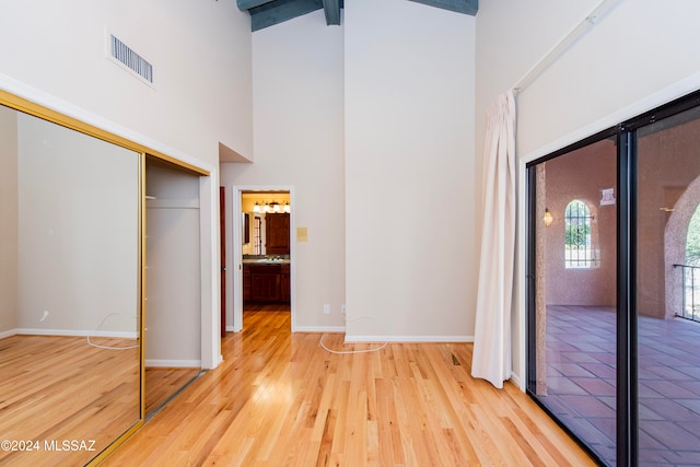 unfurnished bedroom with beamed ceiling, light hardwood / wood-style flooring, high vaulted ceiling, and a closet