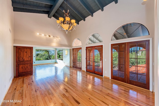 foyer entrance with high vaulted ceiling, french doors, beam ceiling, a notable chandelier, and light hardwood / wood-style floors