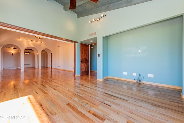 empty room featuring beamed ceiling, high vaulted ceiling, track lighting, and light wood-type flooring