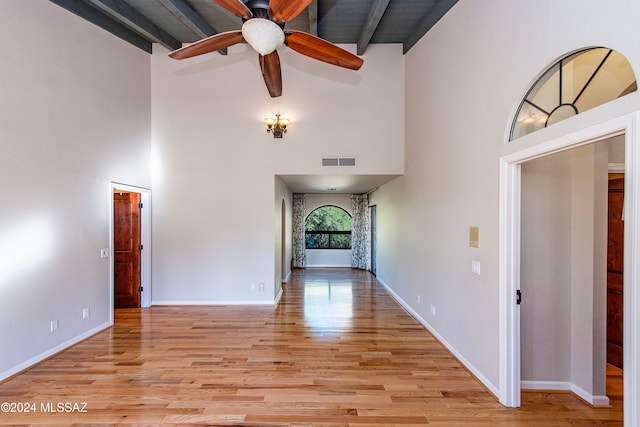 unfurnished living room featuring beamed ceiling, ceiling fan, light hardwood / wood-style floors, and high vaulted ceiling