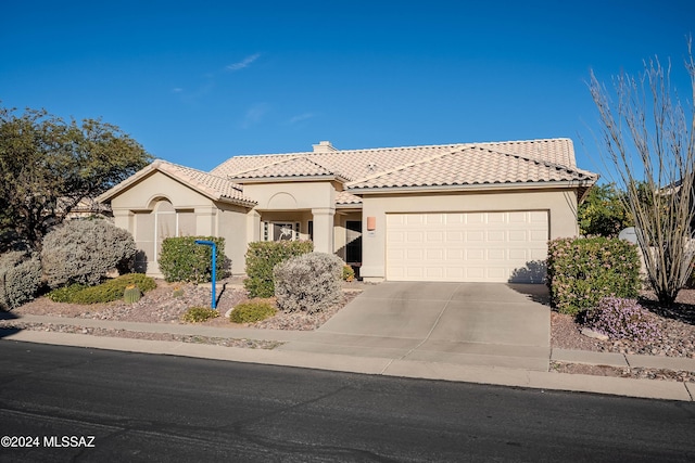 mediterranean / spanish house featuring a garage, concrete driveway, a tile roof, a chimney, and stucco siding