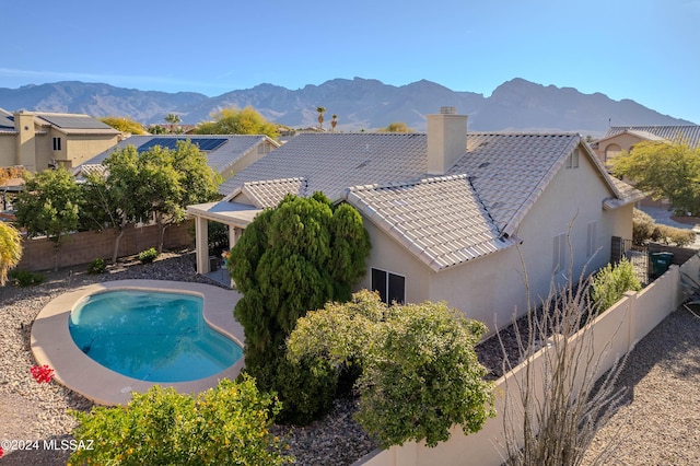 back of house with a fenced in pool, a tile roof, a fenced backyard, a mountain view, and stucco siding