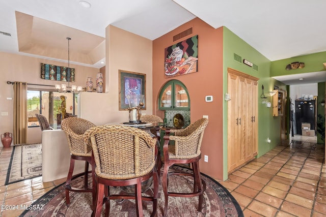 tiled dining space featuring a chandelier, lofted ceiling, and a raised ceiling