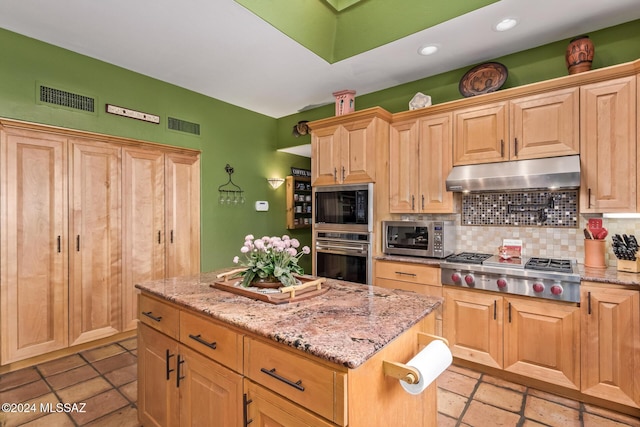 kitchen with light stone countertops, appliances with stainless steel finishes, tasteful backsplash, and a kitchen island