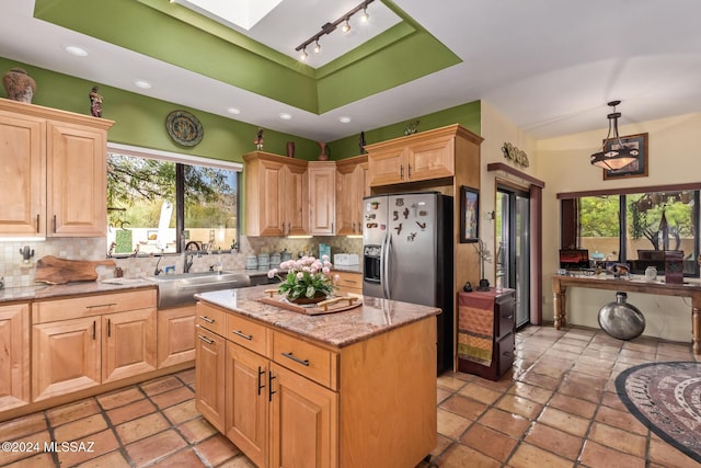 kitchen with pendant lighting, a kitchen island, sink, stainless steel fridge, and a raised ceiling