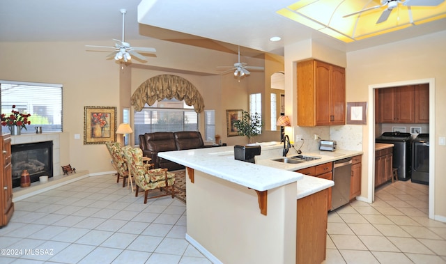 kitchen with sink, stainless steel dishwasher, kitchen peninsula, a kitchen bar, and washer and dryer