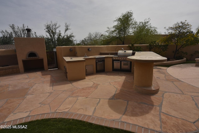 view of patio featuring a grill, a fireplace, an outdoor kitchen, and fence