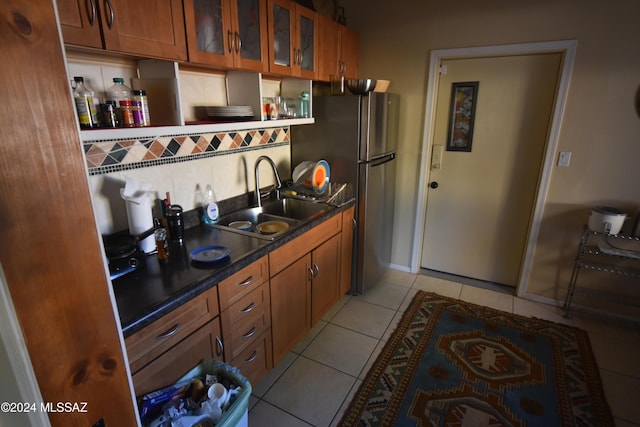 kitchen with freestanding refrigerator, a sink, brown cabinetry, and decorative backsplash
