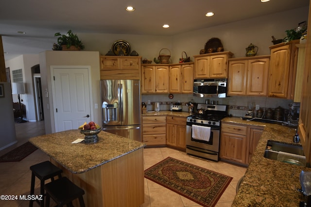 kitchen featuring decorative backsplash, light stone countertops, stainless steel appliances, sink, and a kitchen island