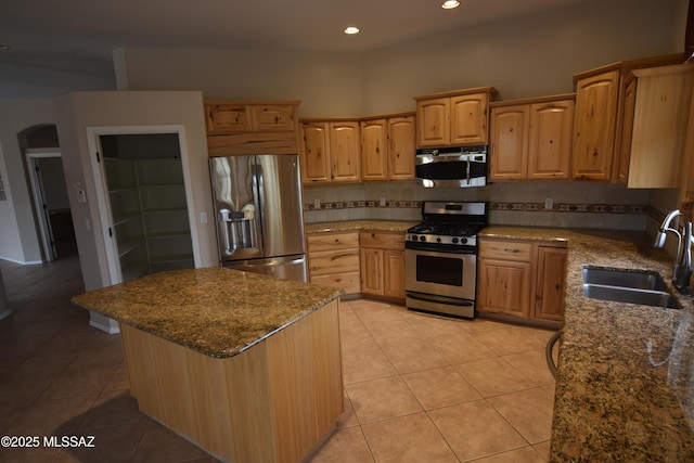 kitchen with light tile patterned flooring, a sink, stainless steel appliances, arched walkways, and decorative backsplash