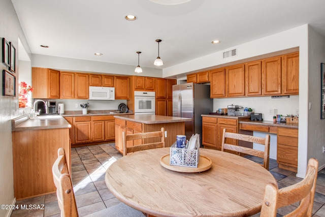 kitchen featuring stainless steel fridge, a kitchen island, hanging light fixtures, and sink