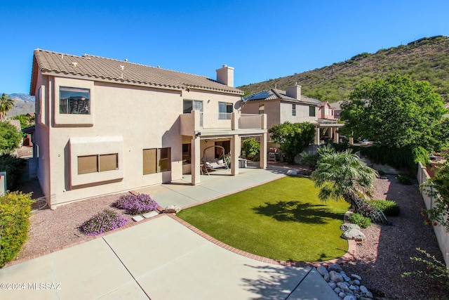 rear view of property featuring a lawn, a mountain view, a balcony, and a patio