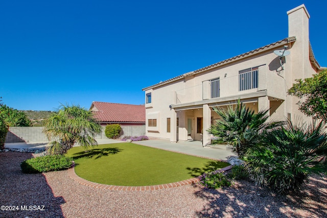 rear view of house with a balcony, a yard, and a patio