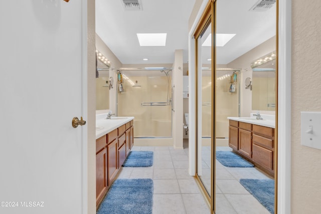 bathroom featuring vanity, a shower with door, a skylight, tile patterned flooring, and toilet