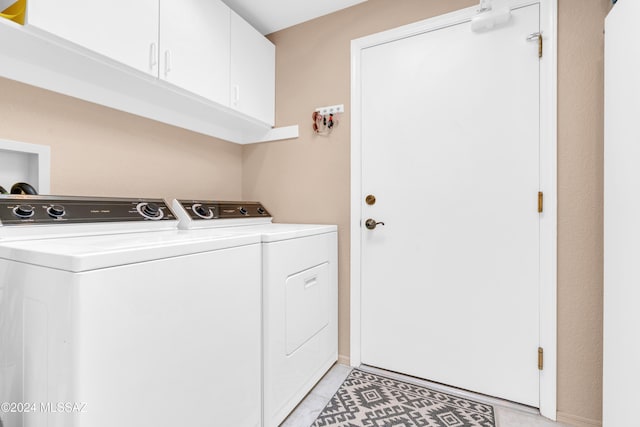 clothes washing area featuring washer and dryer, light tile patterned flooring, and cabinets