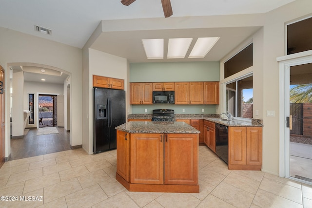 kitchen featuring dark stone countertops, a center island, light tile patterned floors, and black appliances