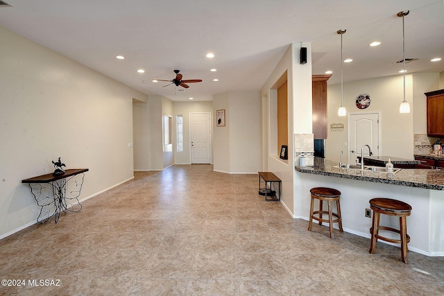 kitchen with kitchen peninsula, ceiling fan, pendant lighting, a breakfast bar, and sink