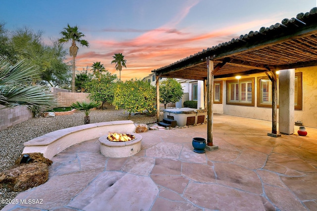 patio terrace at dusk featuring an outdoor fire pit and a hot tub