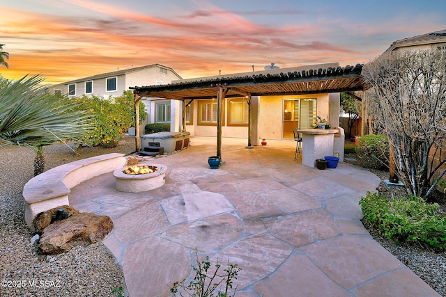 back house at dusk featuring a patio area, a hot tub, an outdoor bar, an outdoor fire pit, and a pergola