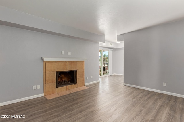 unfurnished living room with wood-type flooring and a tiled fireplace