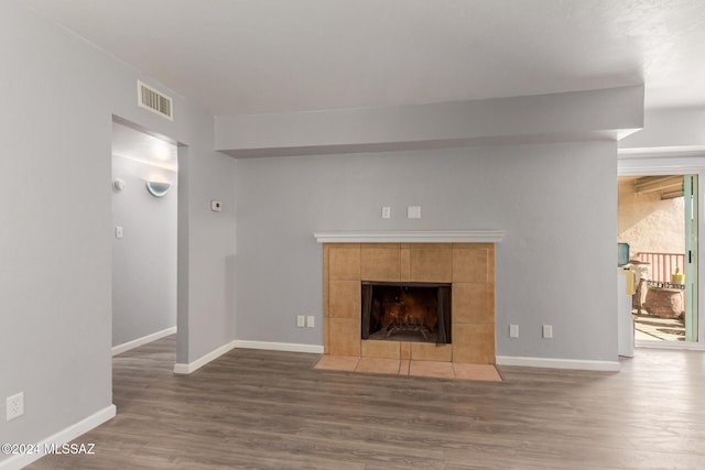 unfurnished living room with a tiled fireplace and dark hardwood / wood-style flooring