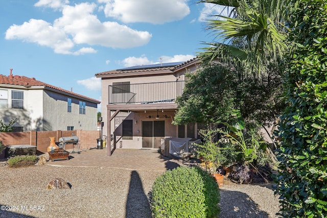 back of property with ceiling fan, a balcony, a patio, and solar panels