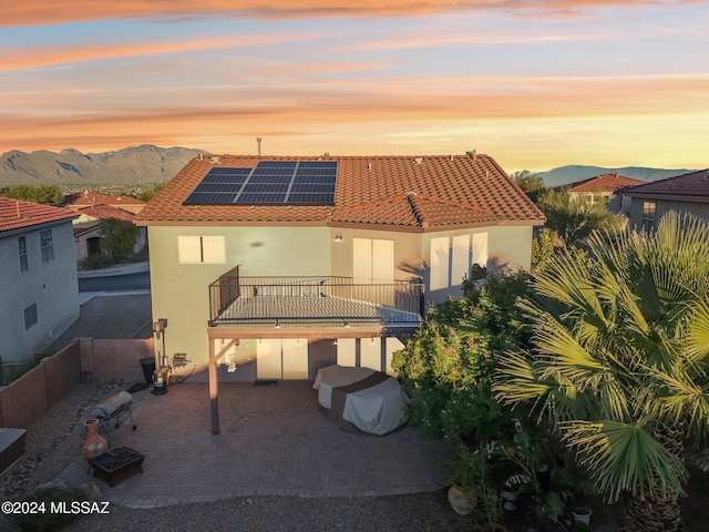 back house at dusk with a patio area, a mountain view, a balcony, and solar panels