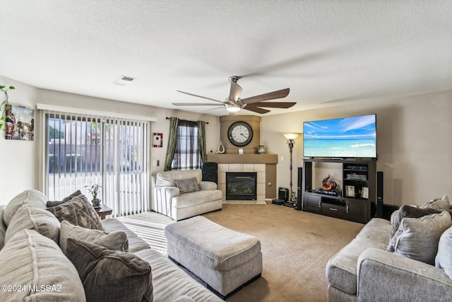 carpeted living room featuring a textured ceiling, ceiling fan, and a tiled fireplace