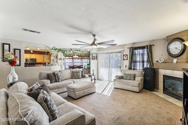 carpeted living room with a tiled fireplace, ceiling fan, and a textured ceiling