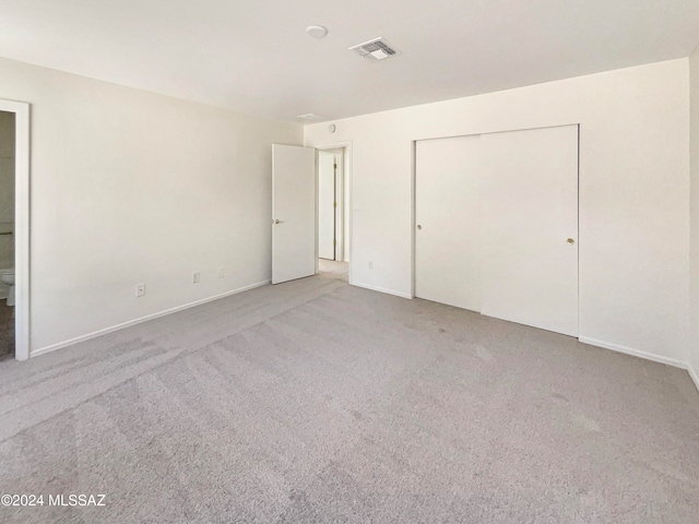 unfurnished bedroom featuring a closet, light carpet, and ensuite bath